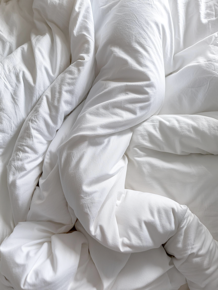 Close-up of crumpled white bedsheets and pillowcases on a bed.