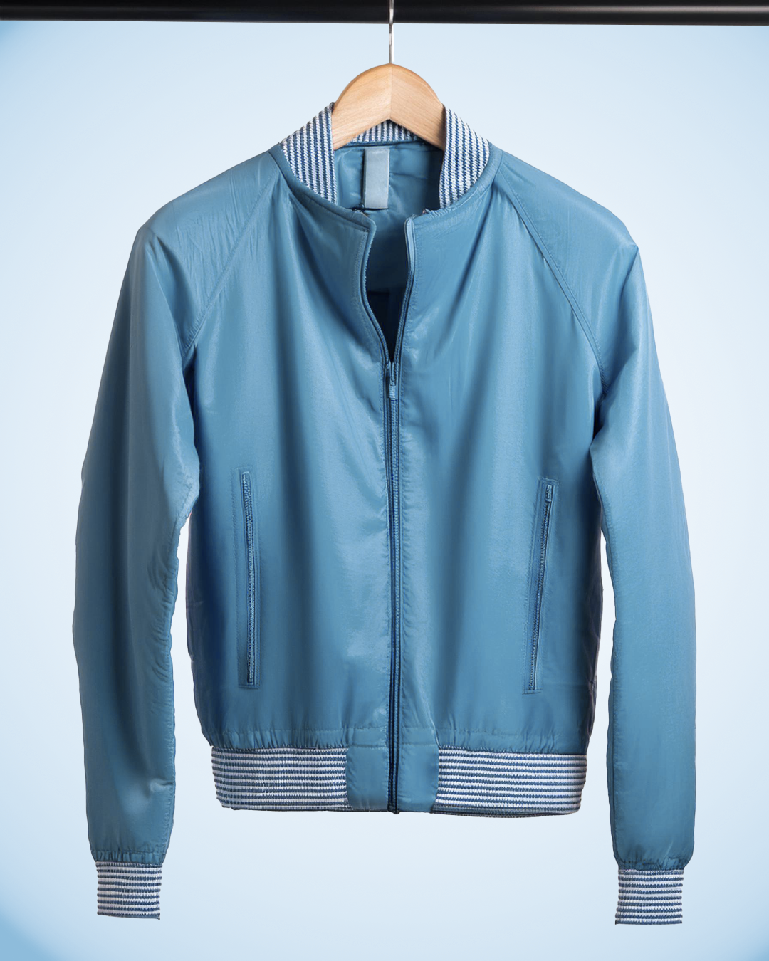 Light blue bomber jacket hanging on a wooden hanger against a light background.