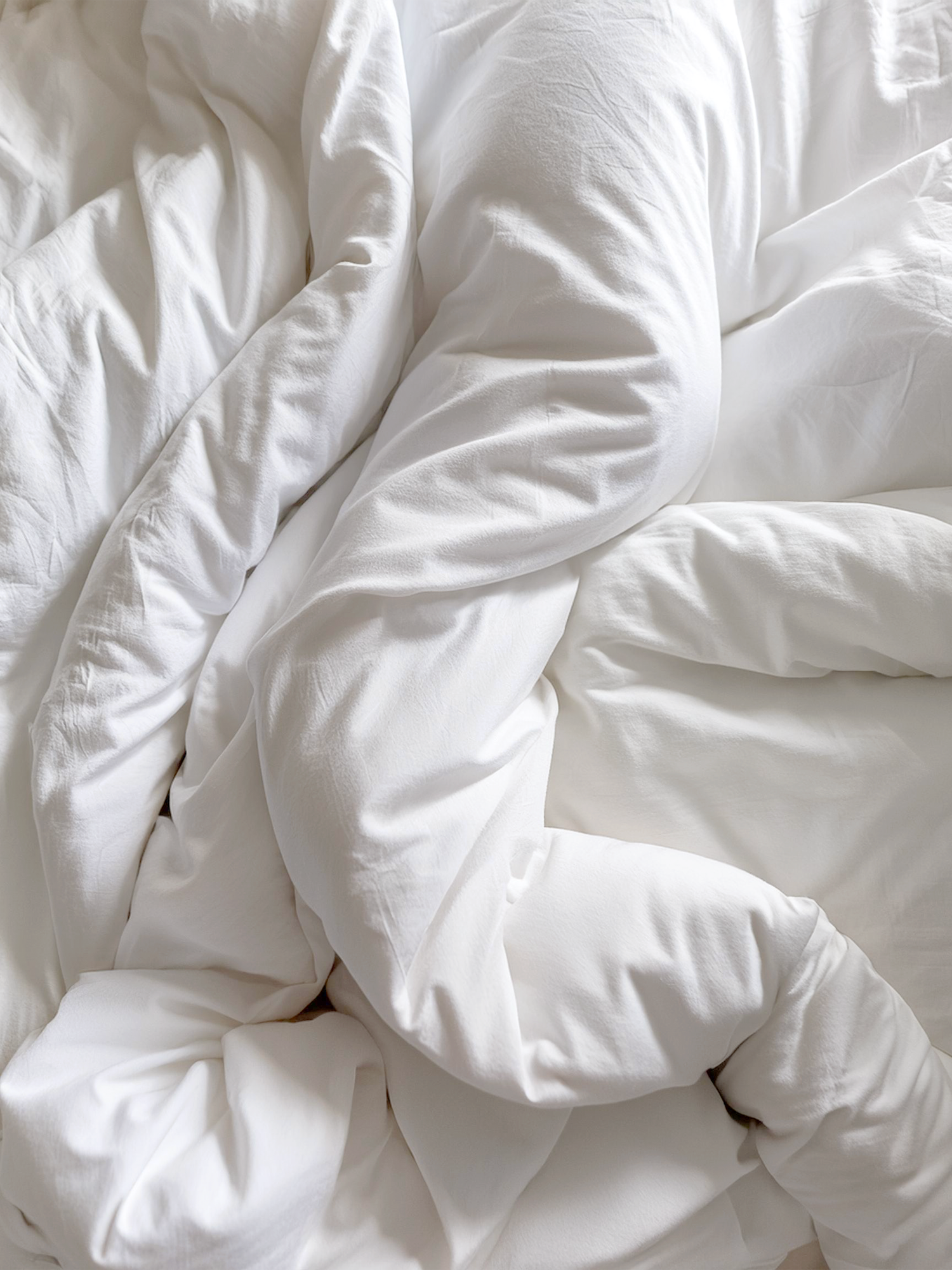 Close-up of a rumpled white bed with soft, wrinkled sheets and pillows.