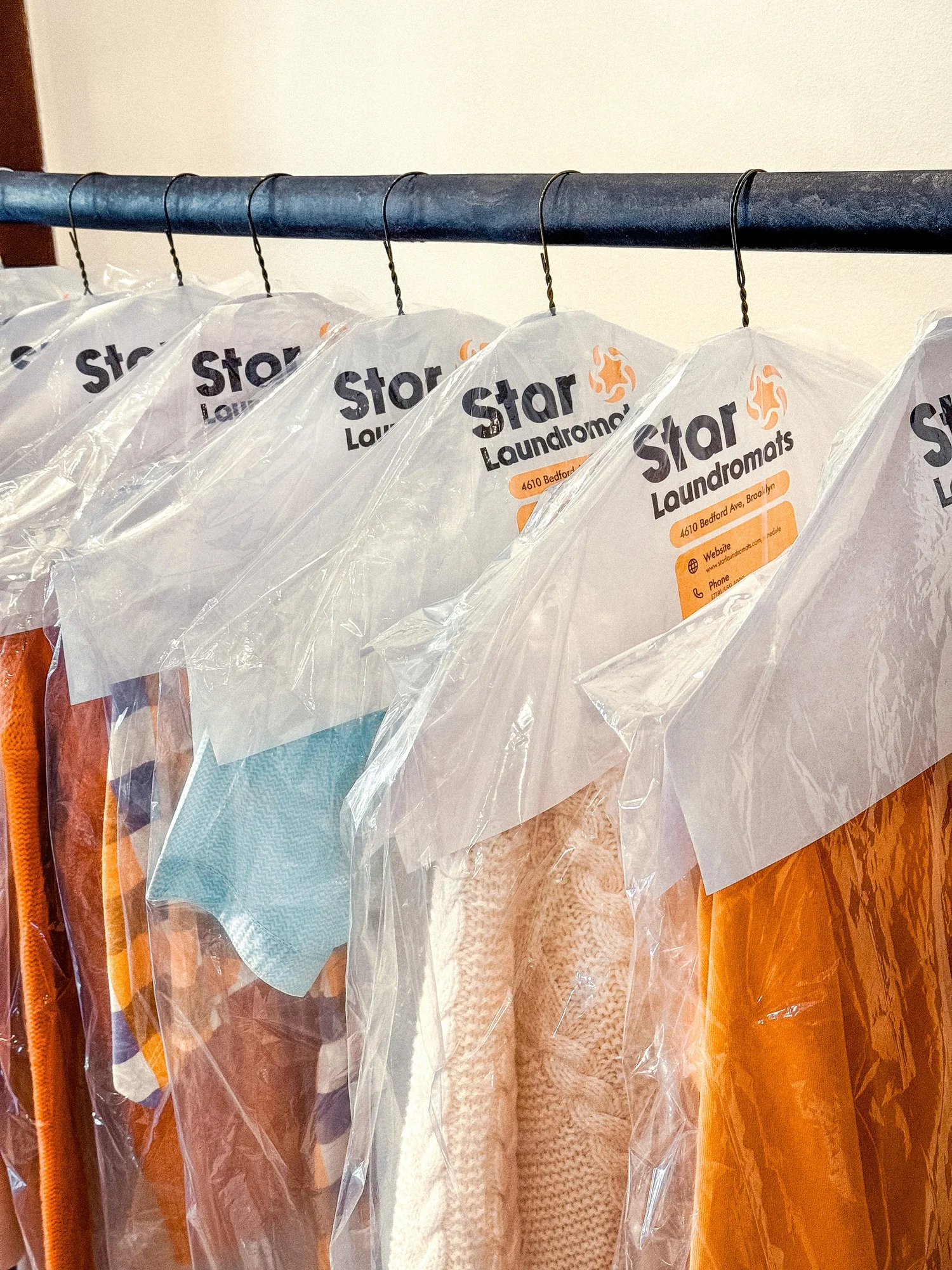 Clothing items wrapped in plastic bags hanging on a metal rod at Star Laundromats.