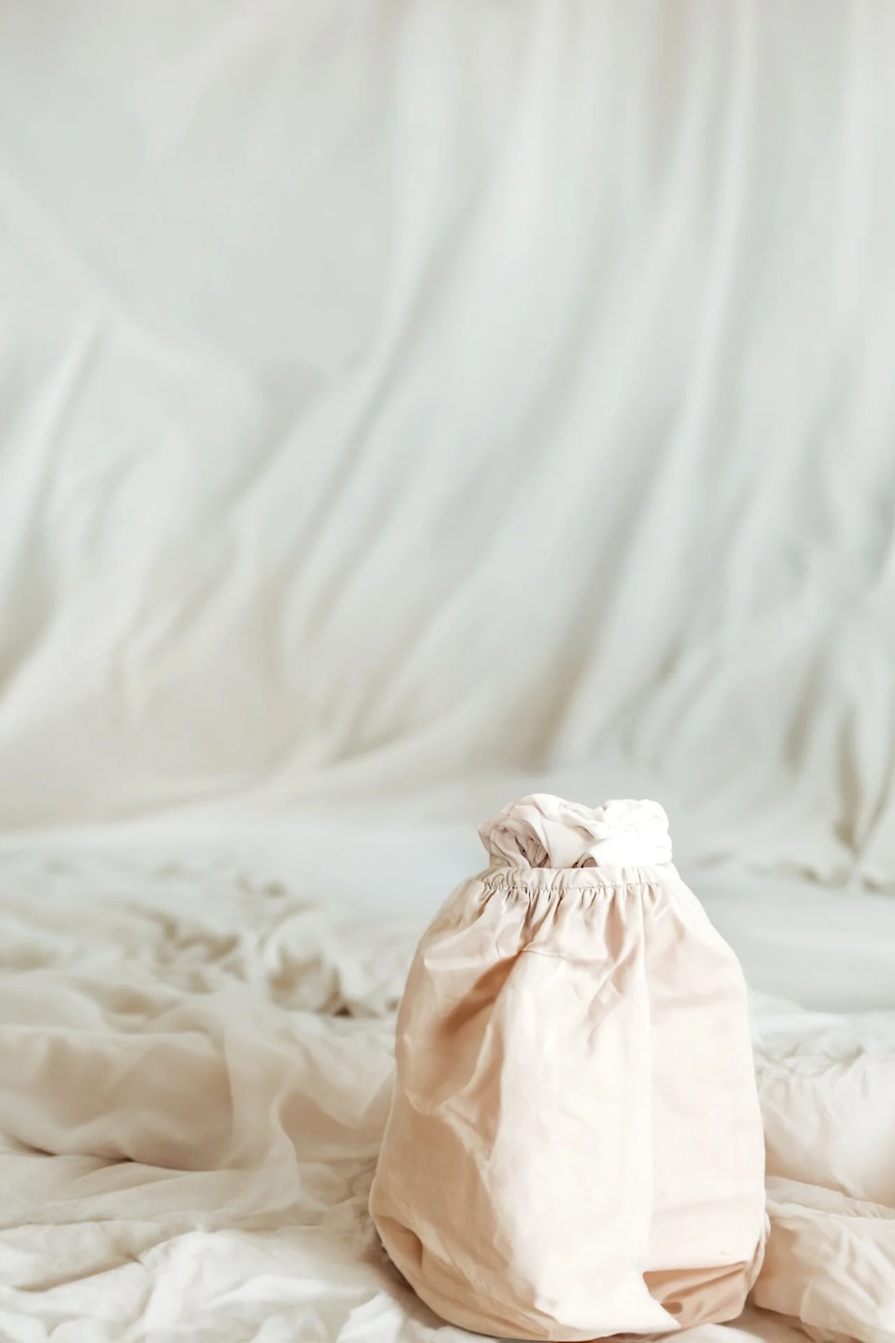 A soft, beige drawstring bag on a white textured fabric background.