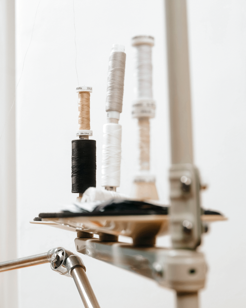 Several spools of thread in black, beige, white, and light beige on a sewing machine stand.