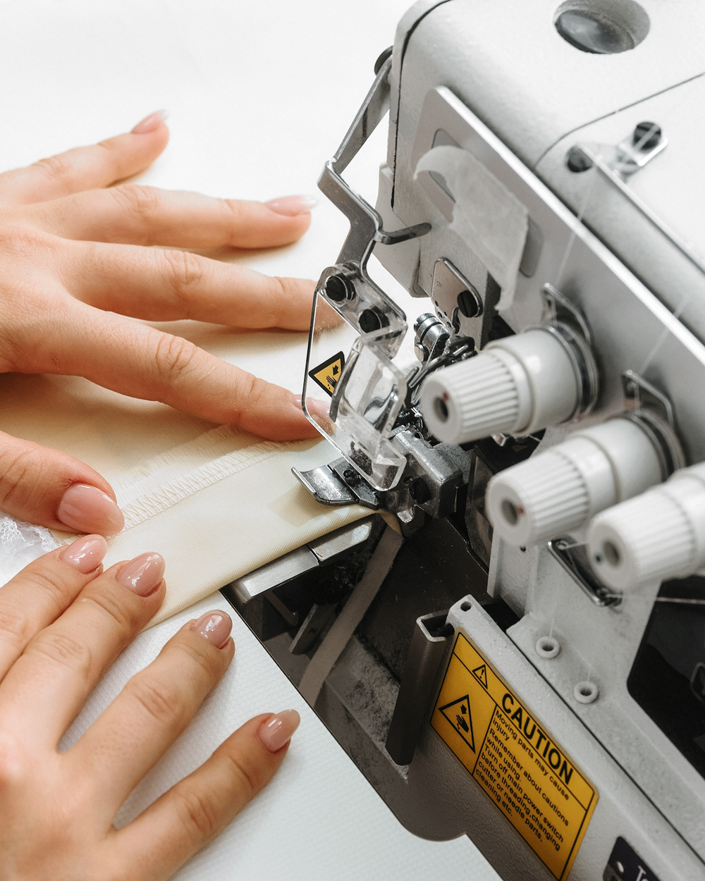 Close-up of hands guiding fabric through a sewing machine during sewing process.