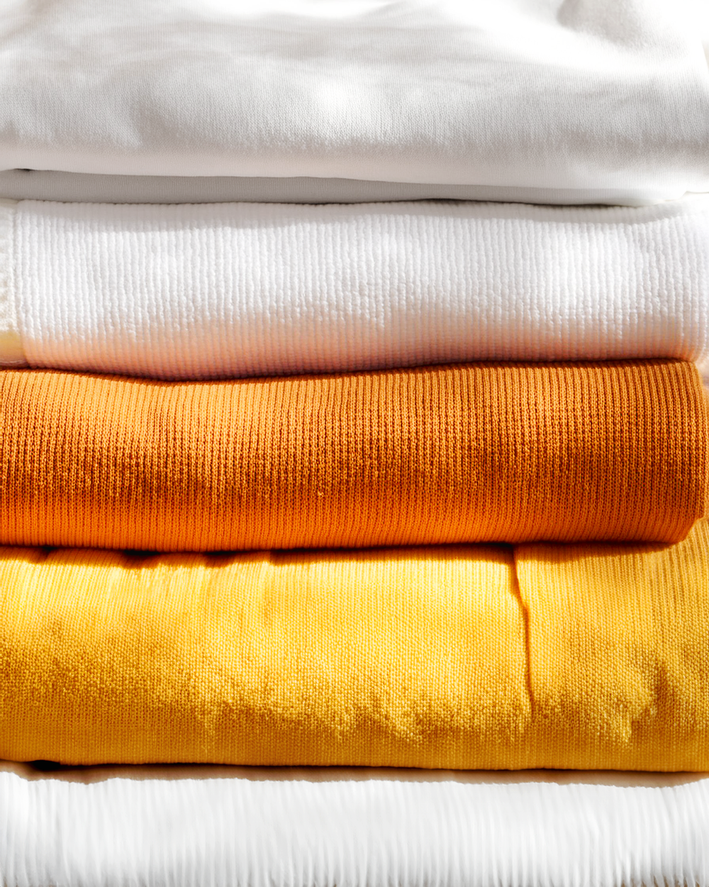 Stack of folded clothing in white, cream, orange, and yellow colors.