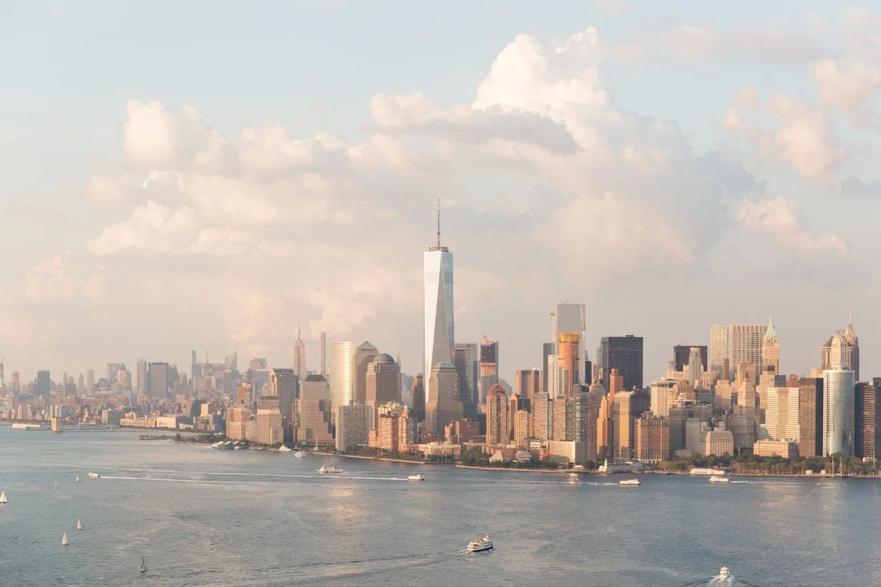 City skyline of Manhattan, New York, viewed from across the waterfront with boats sailing on the river in the foreground.