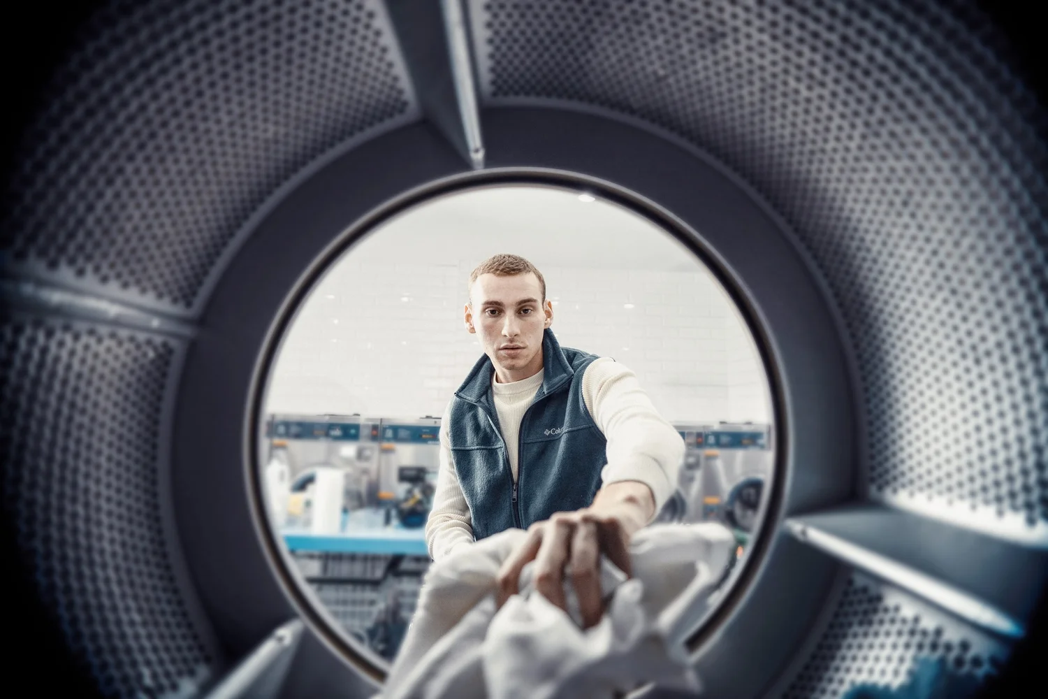 Young man loading laundry into a front-loading washing machine in a laundromat.